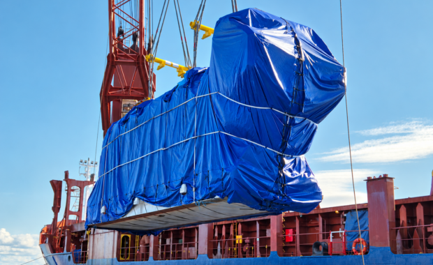Oversized power plant cargo wrapped in blue tarpaulin during heavy-lift vessel loading, part of an international project cargo shipment.