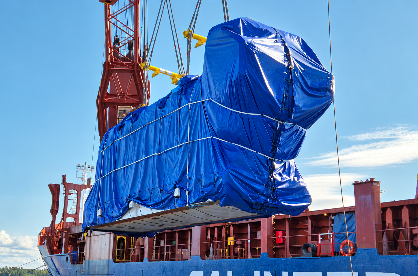 Oversized power plant cargo wrapped in blue tarpaulin during heavy-lift vessel loading, part of an international project cargo shipment.