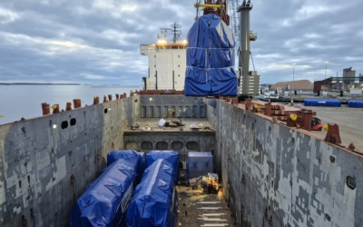 Overhead view of a vessel's cargo hold with power plant units already stowed and another oversized unit lowered into place by crane.