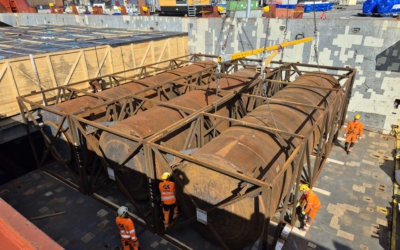 Large steel components in open crating frames inside a ship's hold, part of an oversized cargo shipment for a power plant project.