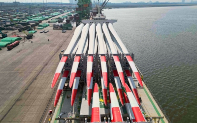 View down the loaded deck toward the stern, blade roots lined up in cradles beside the river and a port crane