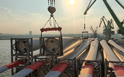 Close-up at sunset of a crane lowering a lifting frame onto a blade root secured in its steel cradle on deck