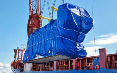 Oversized power plant cargo wrapped in blue tarpaulin during heavy-lift vessel loading, part of an international project cargo shipment.