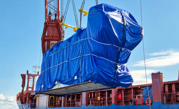 Oversized power plant cargo wrapped in blue tarpaulin during heavy-lift vessel loading, part of an international project cargo shipment.