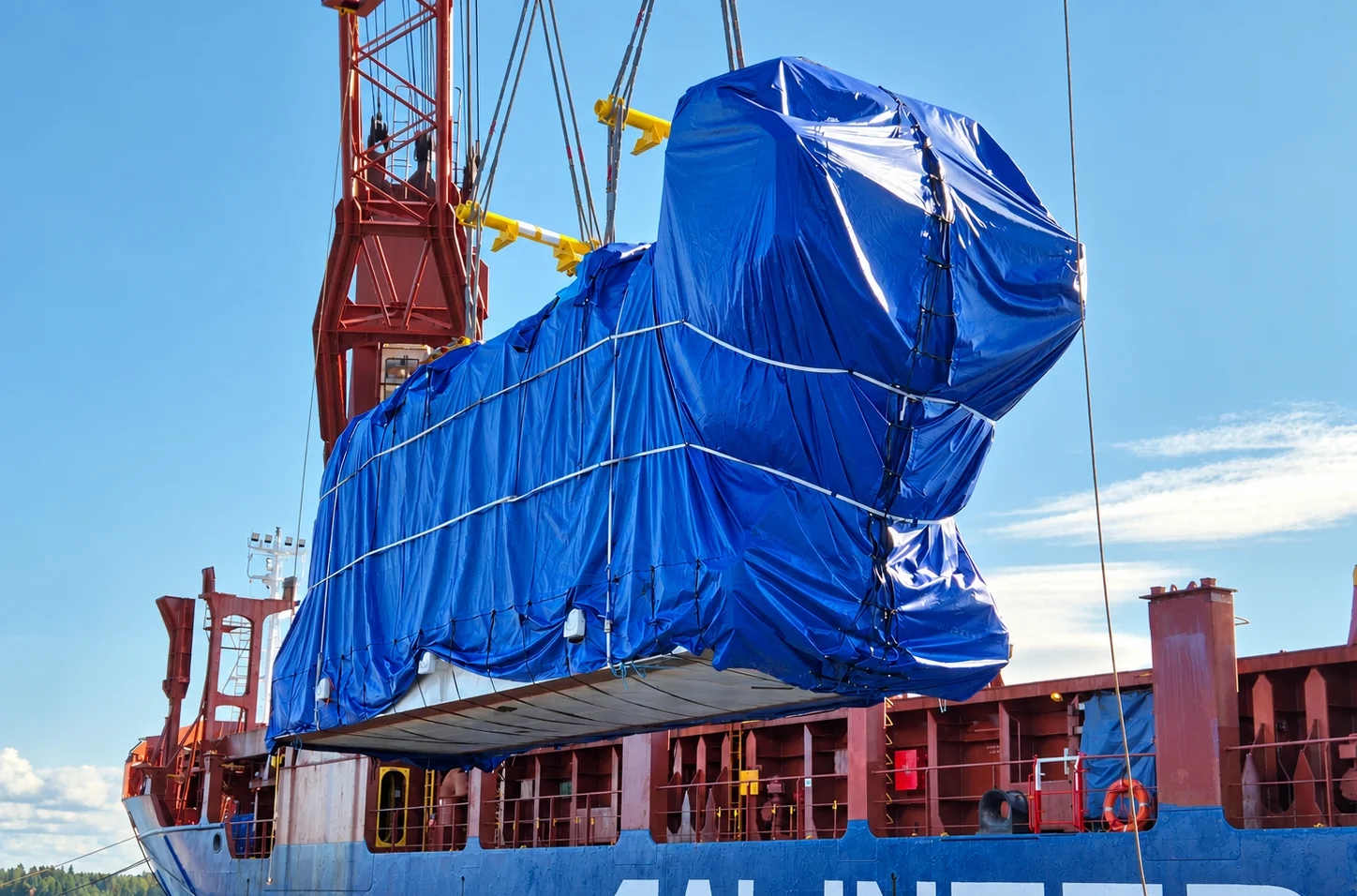 Oversized power plant cargo wrapped in blue tarpaulin during heavy-lift vessel loading, part of an international project cargo shipment.