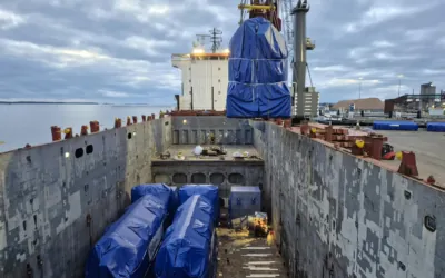 Overhead view of a vessel's cargo hold with power plant units already stowed and another oversized unit lowered into place by crane.